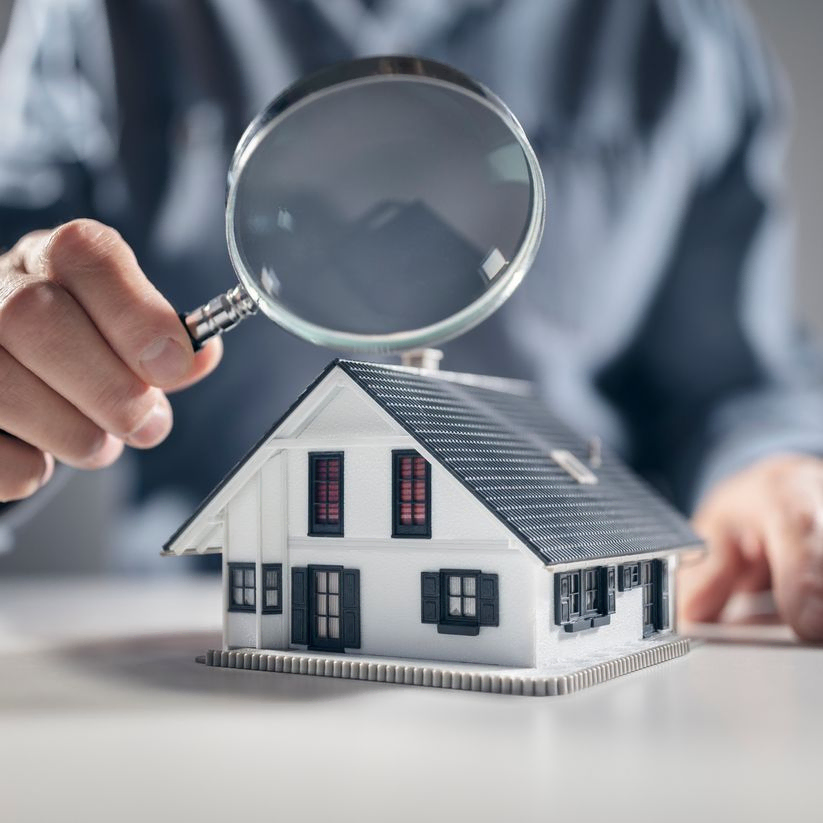 Man with magnifying glass looking at model of house